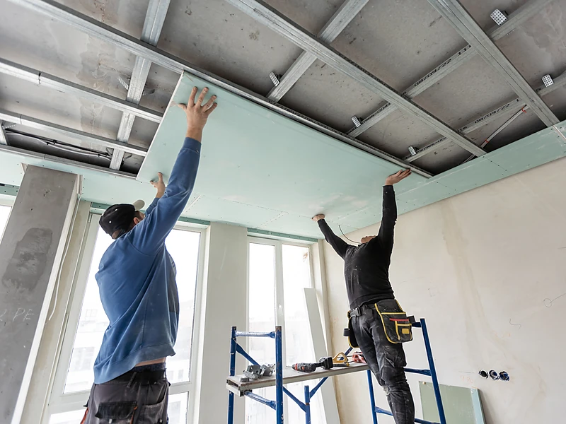 Crew fitting a drywall panel into a suspended ceiling grid on a commercial job